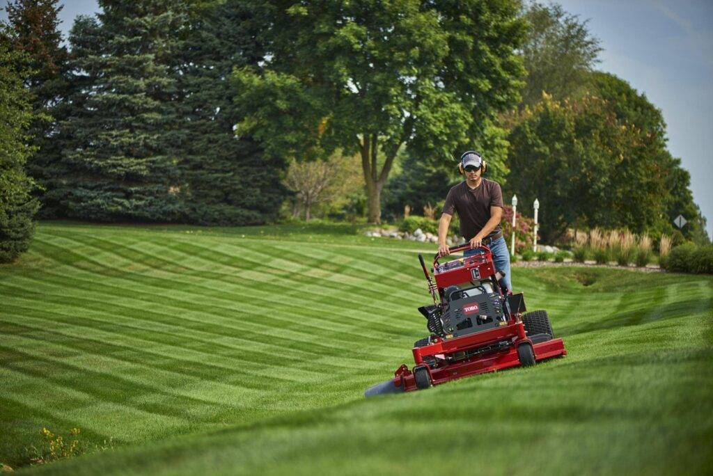 Man operating a red commercial zero-turn mower on a well-manicured lawn.