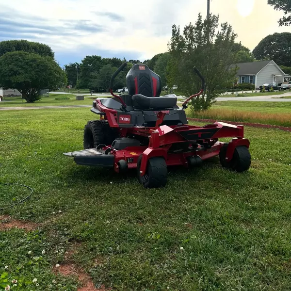 Red zero-turn mower parked on green grass, showcasing its design and features, relevant to lawn care and mowing efficiency for residential and commercial properties.