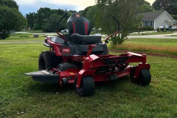Red lawn mower parked on green grass, showcasing its vibrant color in a residential landscape, representing Powerline Equipment's outdoor power equipment offerings for Gratz residents.